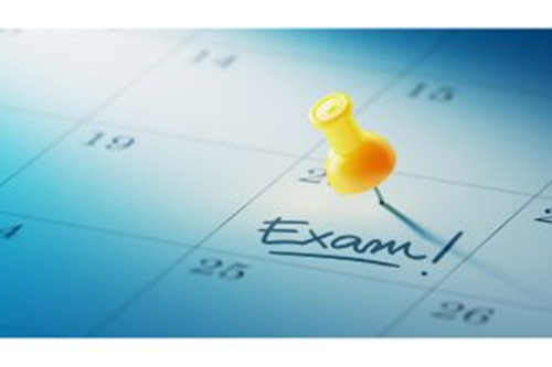 A close up of a calendar with a yellow thumbtack and the word Exam written on the 20th. 